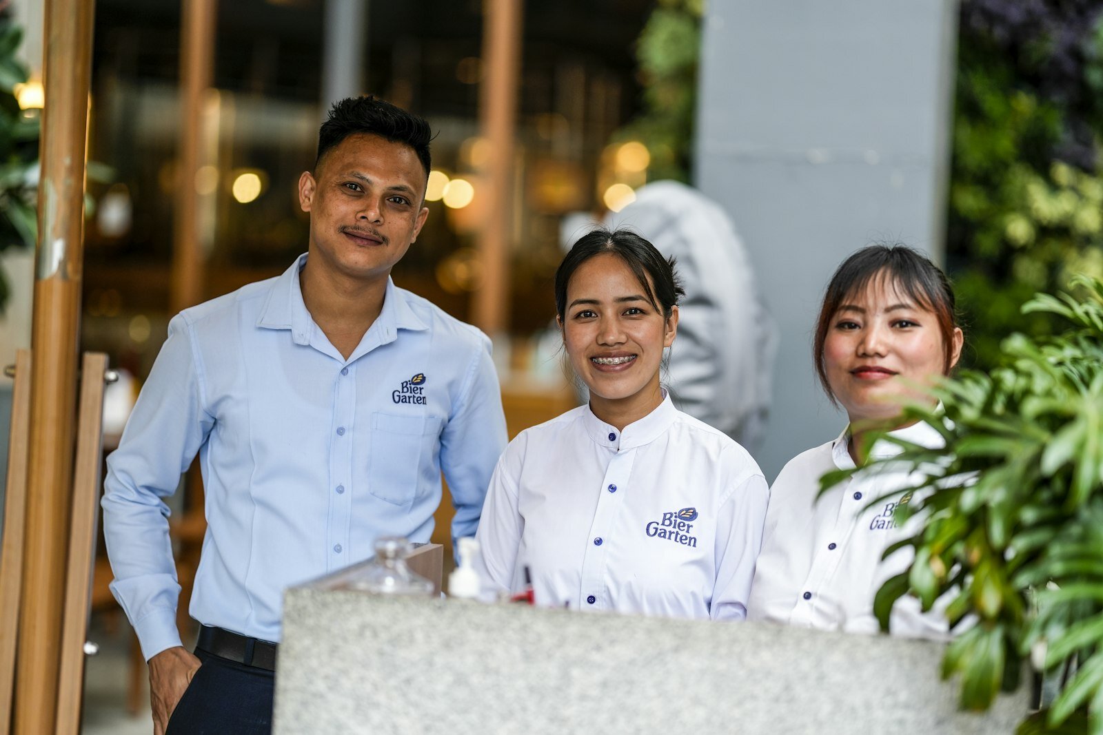 Three smiling restaurant staff members stand behind a counter.