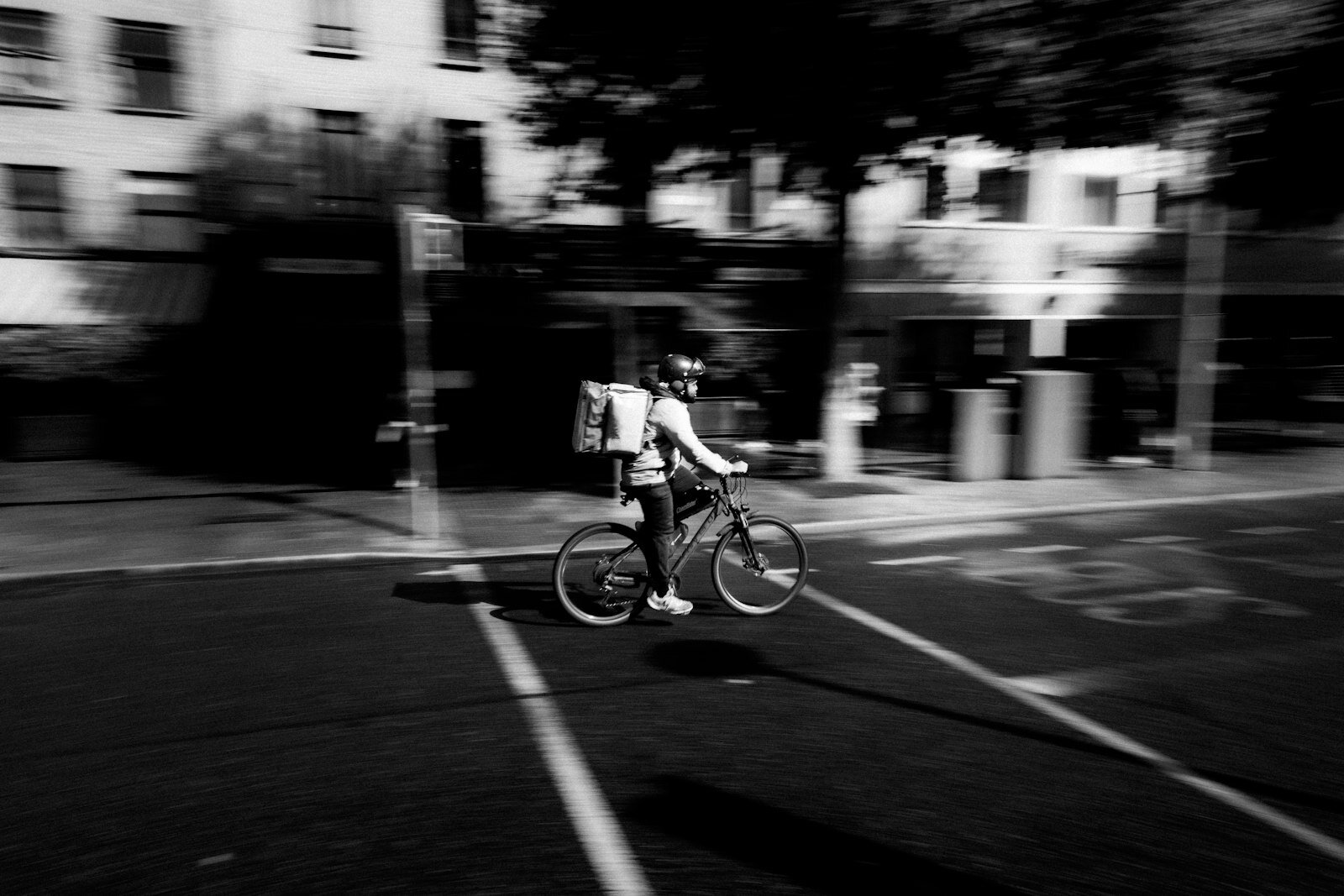 A delivery rider cycles quickly through a blurred city street.